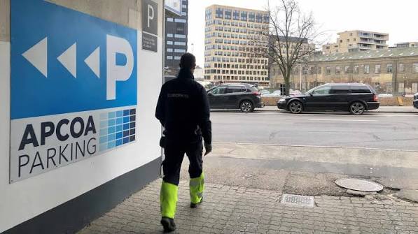 Parkeringsvagt i uniform gående forbi et APCOA PARKING-skilt ved et parkeringsanlæg
