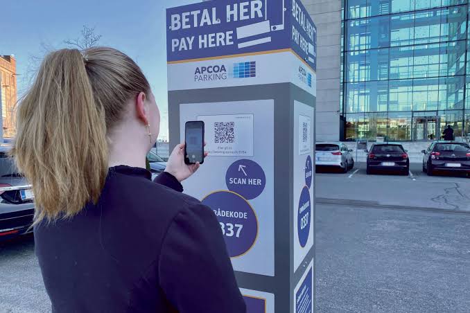 Kvinde der scanner QR-kode på en APCOA PARKING betalingsstander med sin smartphone