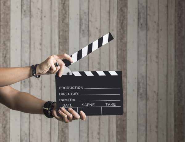 Hands holding a film clapperboard in front of a wooden background – Financial management of film productions via Dynamics NAV job module
