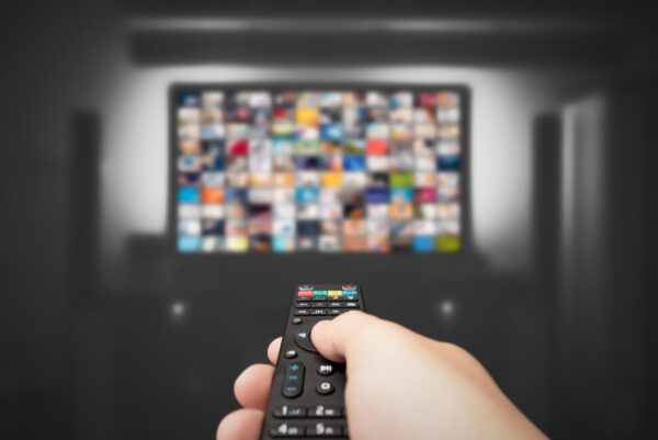 Hand pointing a remote control at a TV screen with media content – Miso Film cloud ERP case at Corpital

